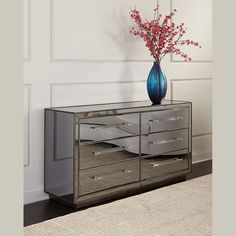 a blue vase with flowers on top of a silver dresser