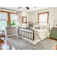 a bed room with a neatly made bed next to two windows and a rug on the floor