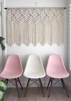 three pink and white chairs in front of a macrame wall hanging