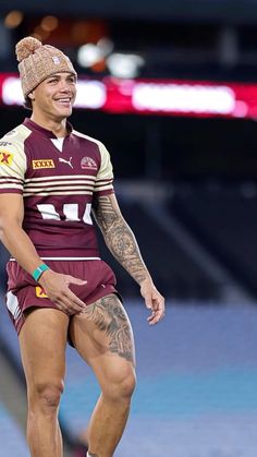 a rugby player in maroon and white uniform with tattoos on his leg, smiling at the camera