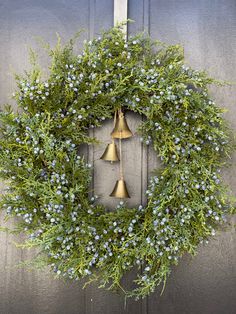 a wreath with bells hanging on the side of a door decorated with blue flowers and greenery