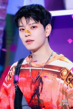 a young man with black hair and piercings on his face is standing in front of a colorful background