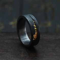 a black and gold wedding band with yellow flowers inlayed to the side, on a wooden surface