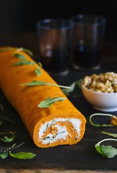 a rolled up food item sitting on top of a table next to a bowl of nuts