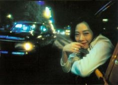 a woman sitting in the drivers seat of a car on a city street at night