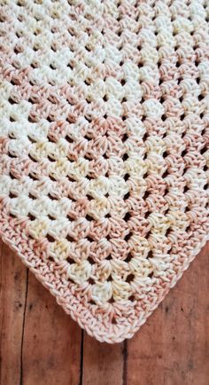 a pink and white crocheted blanket sitting on top of a wooden floor