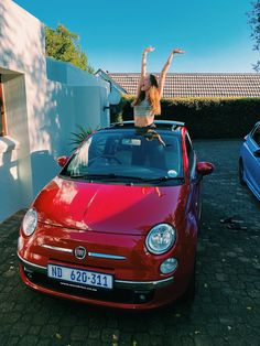 a woman standing on the hood of a red car with her arms in the air