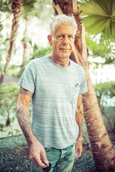 an older man with tattoos standing in front of palm trees and holding a frisbee