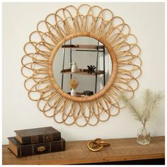 a round mirror sitting on top of a wooden table next to a vase and books
