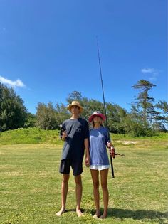 two people standing in the grass holding fishing rods