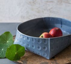 two apples are in a blue bowl on a wooden tray next to a green leaf