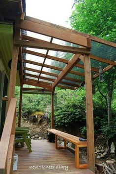 a wooden bench sitting under a pergolated covered patio next to a wooded area