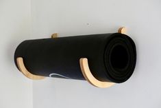 a roll of black yoga mat hanging on a white wall with a wooden holder attached to it