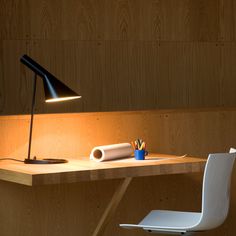 a desk with a lamp on it next to a white chair and a wooden wall