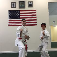 two men standing next to each other with an american flag on the wall behind them