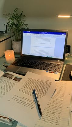 an open laptop computer sitting on top of a desk next to a pile of papers