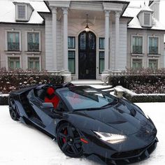 a black sports car is parked in front of a large house with snow on the ground