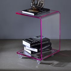 a stack of books sitting on top of a clear shelf next to a silver sculpture