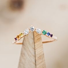 a gold ring with five different colored stones on top of a wooden stand in front of a blurry background