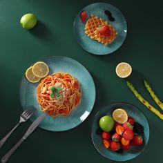 two plates filled with food on top of a green table next to lemons and strawberries