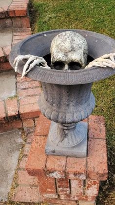 a skull head in a cement planter on brick walkway next to grass and bricks