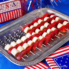 red, white and blue fruit skewers on a tray with american flags in the background