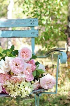 a bouquet of pink flowers sitting on top of a blue bench next to a tree