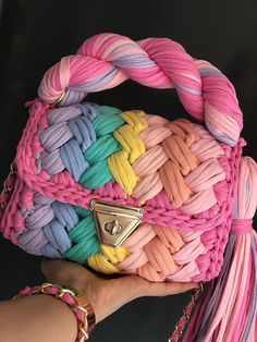 a hand holding a pink, blue, yellow and pink woven purse with gold hardware