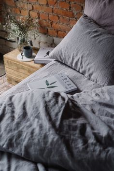 an unmade bed with grey linens, pillows and a plant on the pillow