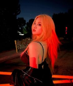 a woman with long blonde hair sitting on a bench in front of the street at night