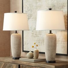 two lamps are sitting on a table next to a vase with flowers in it and a mirror behind them