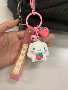 a person holding a pink key chain with an animal on it and a strawberry in the other hand