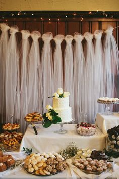 a table topped with lots of desserts next to a wall covered in tulle