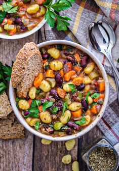 two bowls filled with beans, carrots and bread on top of a wooden table