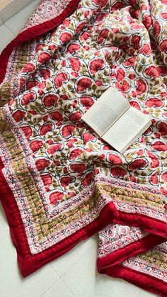 an open book laying on top of a red and white quilted bed coverlet