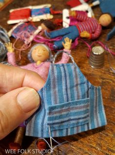 a hand holding a small doll next to other dolls on a table with sewing needles