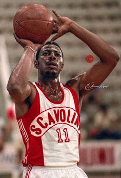 a man holding a basketball in his right hand while wearing a red and white uniform