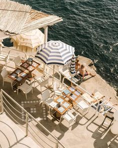 an outdoor dining area with umbrellas and chairs near the water's edge on a sunny day