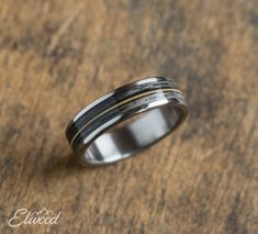 a wedding band with gold and silver inlays on a wooden surface, close up