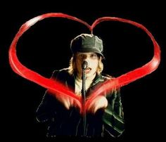 a man holding a microphone in front of a heart shaped red ribbon on a black background