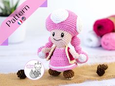 a small crocheted doll is standing next to some pine cones and yarns