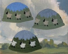 three crocheted hats with sheeps on them are shown in front of a cloudy sky