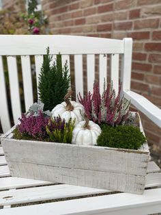 a wooden box filled with plants and white pumpkins sitting on a bench next to a brick wall