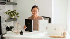 a woman sitting at a desk with two notebooks in front of her and an apple laptop