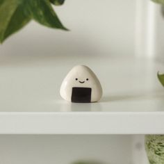 a small white rock with a smiling face on it sitting on a shelf next to a potted plant