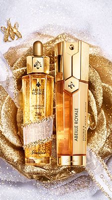 two bottles of perfume sitting next to each other on a white surface with gold foil