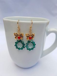 These adorable Christmas Wreath Earrings are Handmade with Emerald Green and Red Swarovski Crystal Bicone Beads and Tierra Cast, Lead-Free Pewter Bow Beads. 14K Gold Filled Ear Wire by Tierra Cast has been used. Meticulously wire wrapped with Tarnish Resistant 14k Gold Plated Wire.  Charming yet Holiday Beaded Jewelry, Christmas Wreath Earrings, Diy Christmas Earrings, Bow Beads, Christmas Jewelry Diy, Wreath Earrings, Crystal Bead Jewelry, Holiday Beading, Earrings Emerald