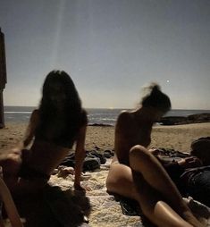 two women are sitting on the beach in their bathing suits