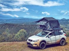 a car with a roof tent on top of it parked in the grass near mountains