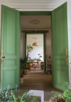 an open green door leading to a dining room with potted plants on the floor